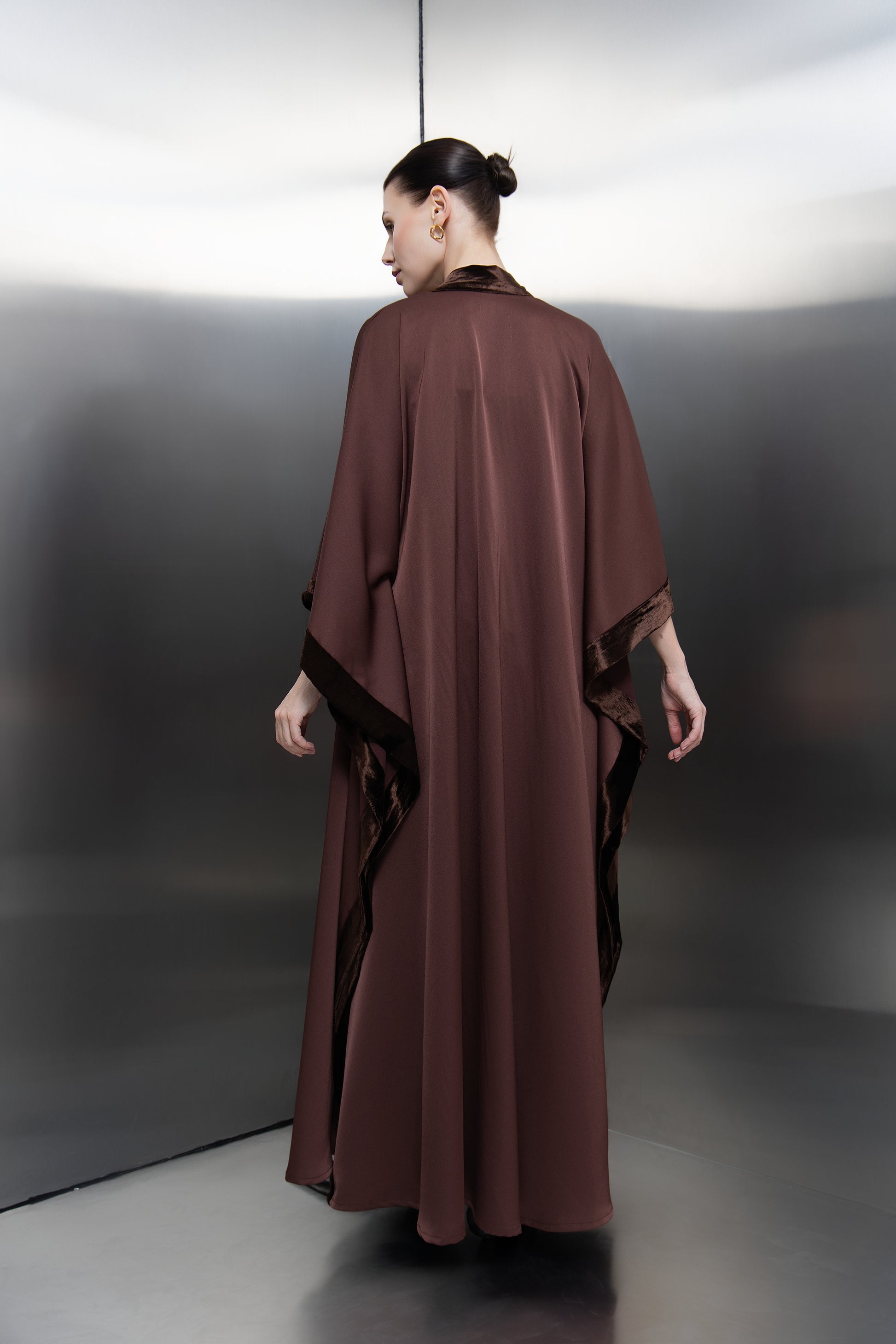 "Back profile of the brown velvet skirt and kimono set by Mona Al Shebil, showcasing the graceful drape of the cape and the structured fit of the luxury evening ensemble."