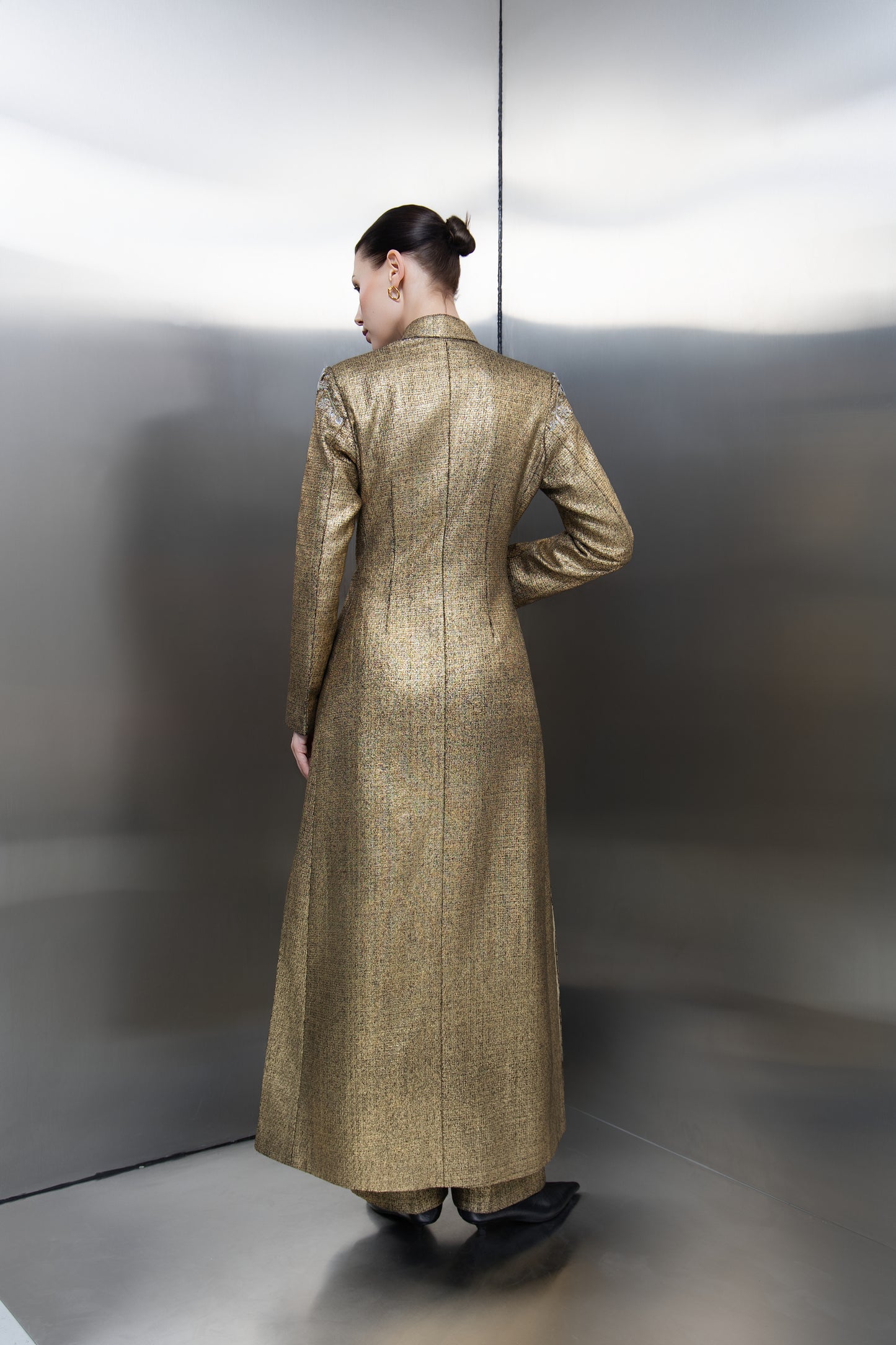 The back profile of the Mona Al Shebil gold structured jacket, highlighting its tailored floor-length silhouette and clean lines that represent modern elegance and professional empowerment for the contemporary woman."
