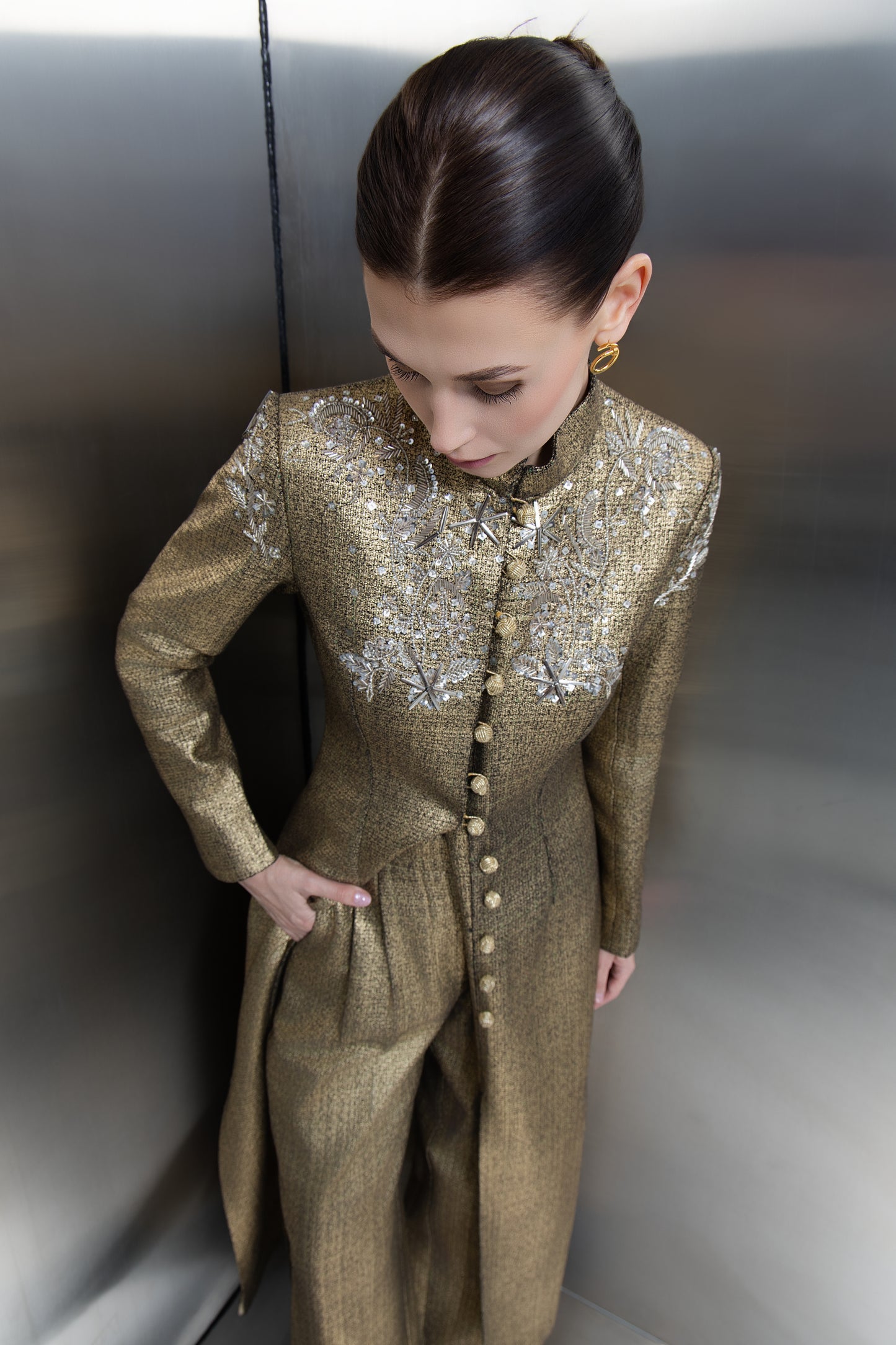 A detailed closeup of the intricate silver floral embroidery and crystal embellishments on the shoulders and collar of the Mona Al Shebil gold jacket, emphasizing premium craftsmanship and timeless luxury design."