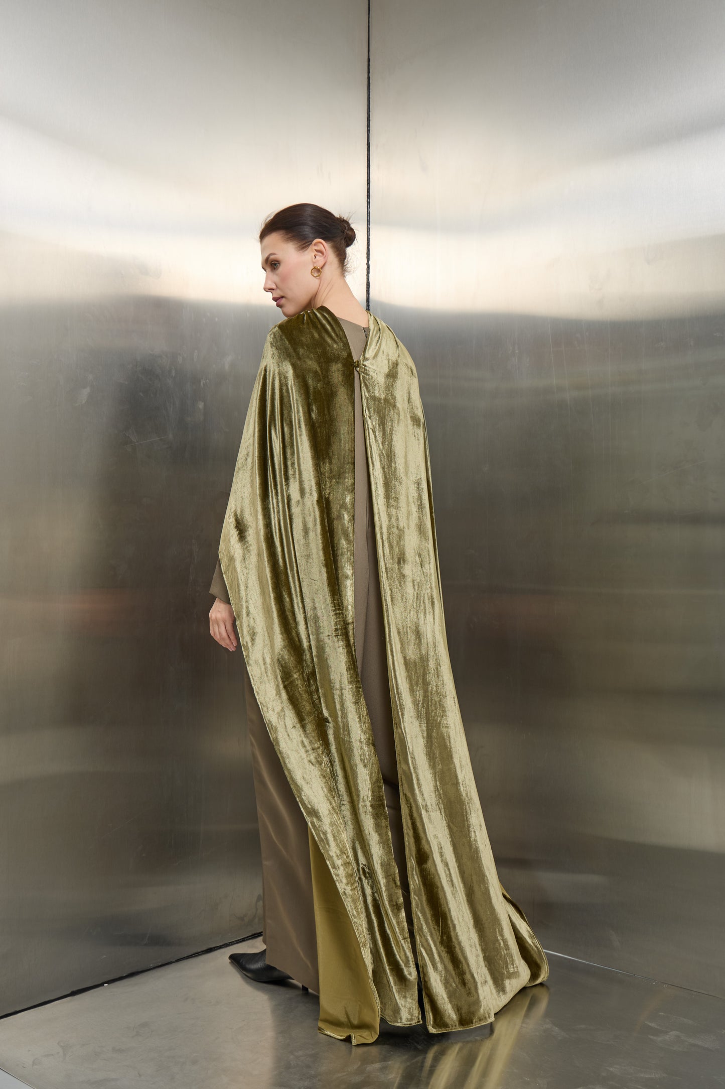 "Back profile of the olive green velvet cape jumpsuit set by Mona Al Shebil, showcasing the floor-length drape of the velvet against the structured jumpsuit design."