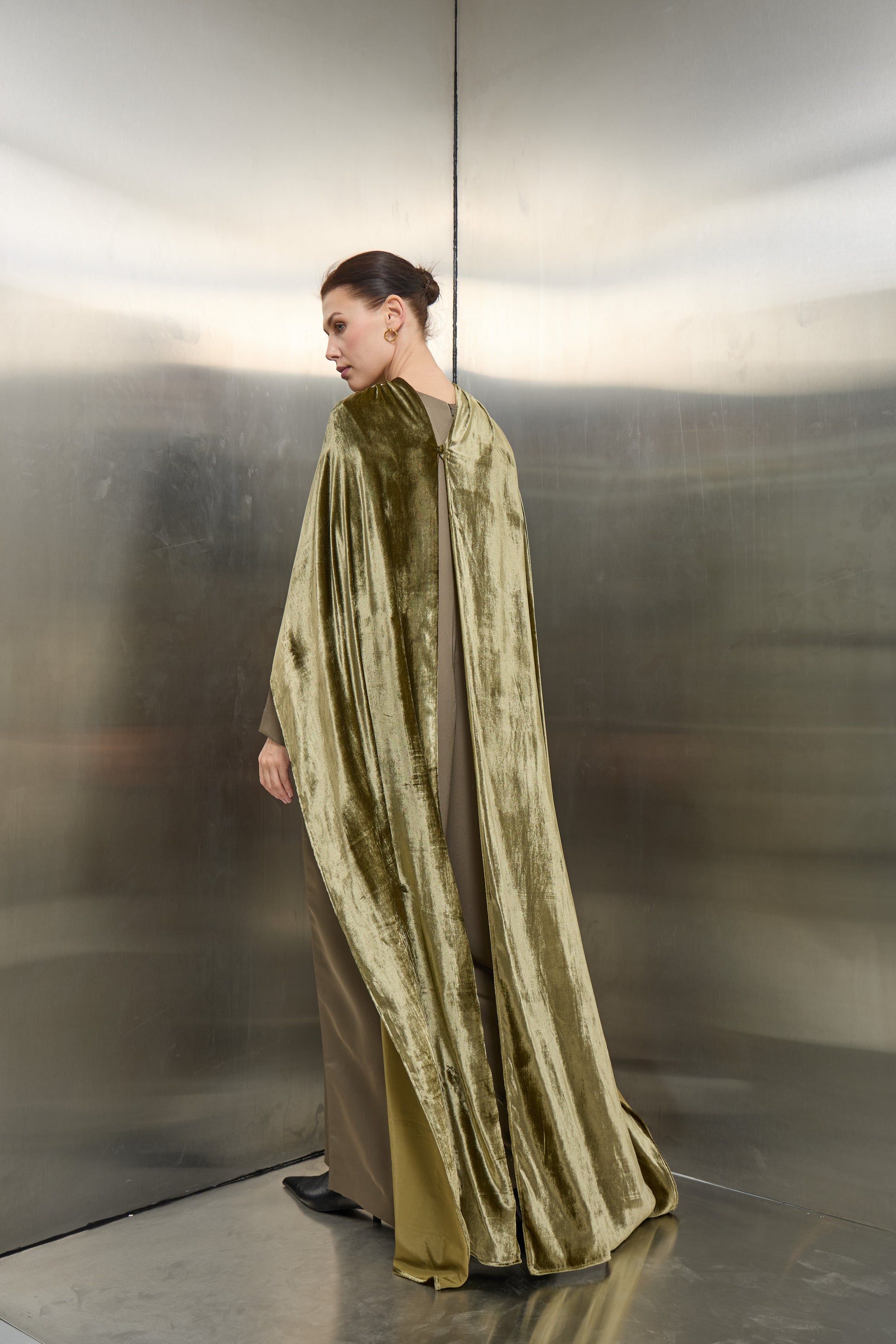 "Back profile of the olive green velvet cape jumpsuit set by Mona Al Shebil, showcasing the floor-length drape of the velvet against the structured jumpsuit design."