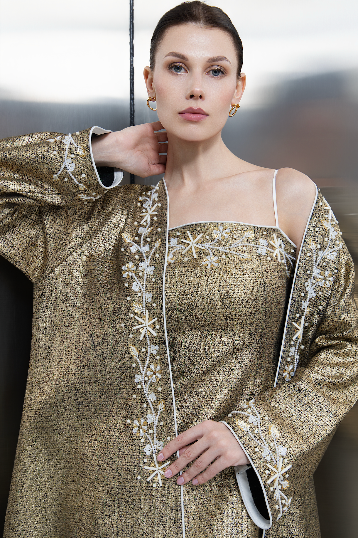 Detailed closeup of silver floral embroidery and crystal embellishments on the metallic gold tweed fabric of a Mona Al Shebil designer jacket, highlighting premium craftsmanship."