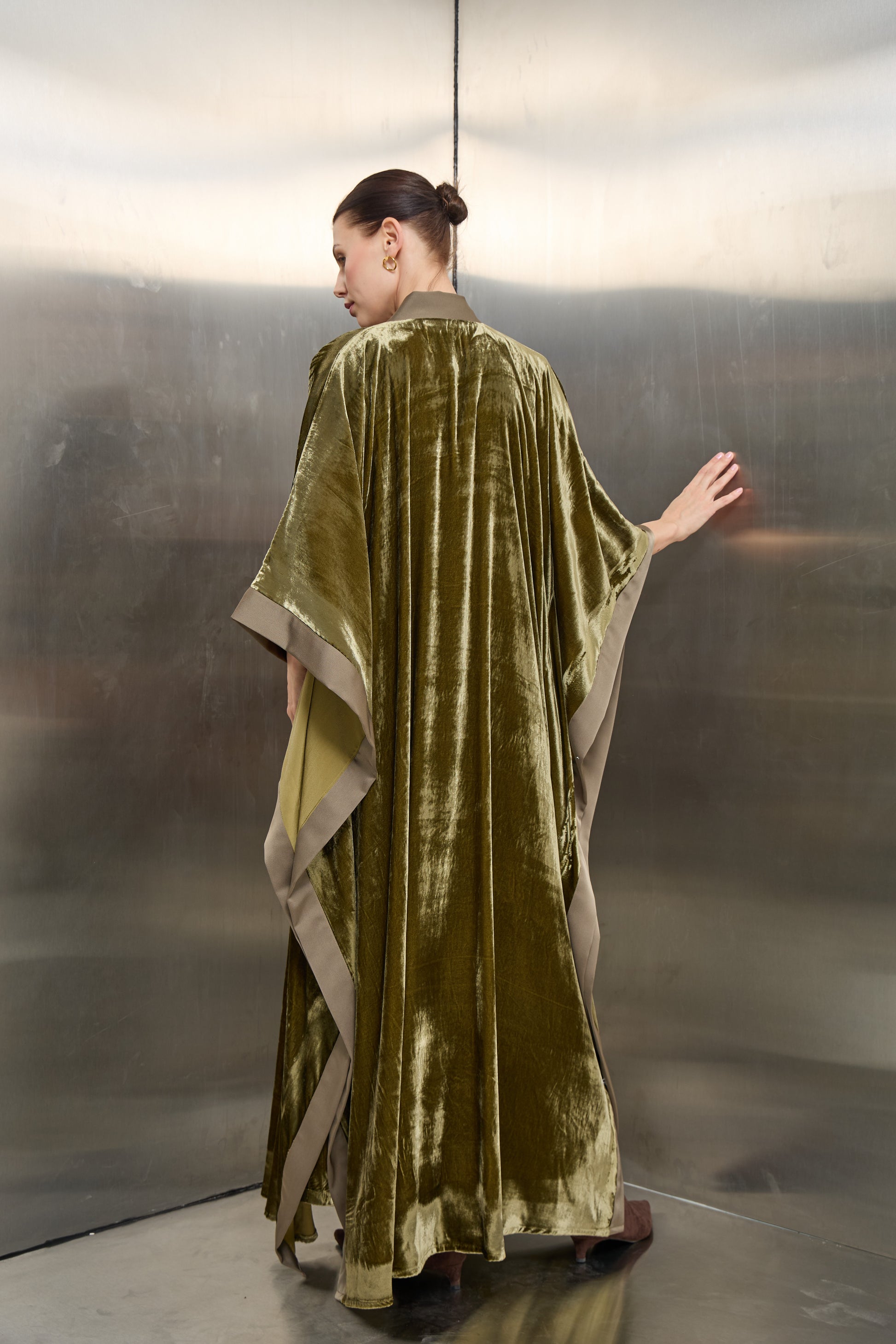 "Rear view of the olive green velvet kaftan by Mona Al Shebil, highlighting the luxurious draped fabric and wide contrasting hem for a sophisticated flow."