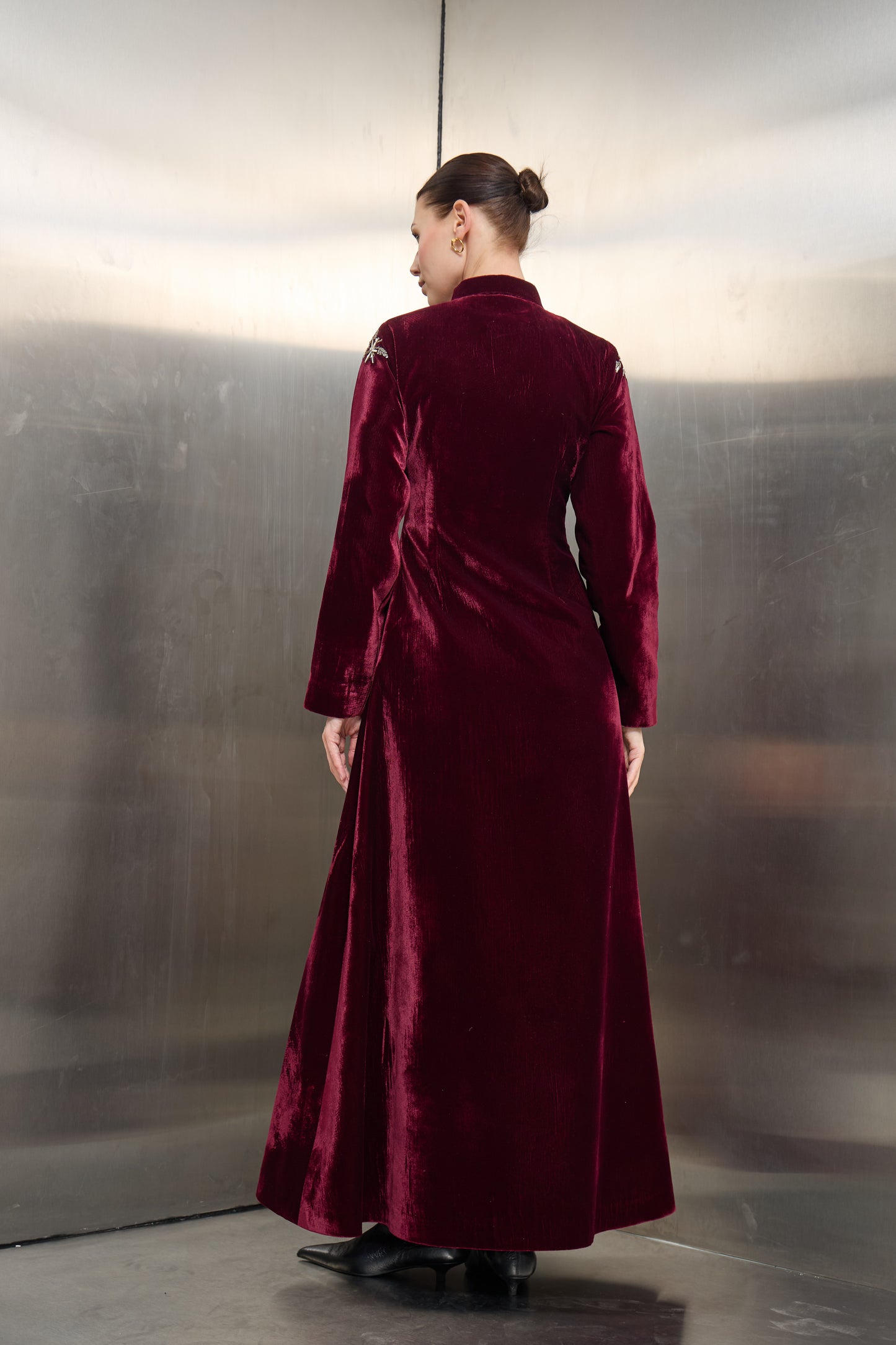 Back profile of the burgundy velvet long jacket by Mona Al Shebil, highlighting the structured floor-length drape and premium velvet finish for high-end modest wear."