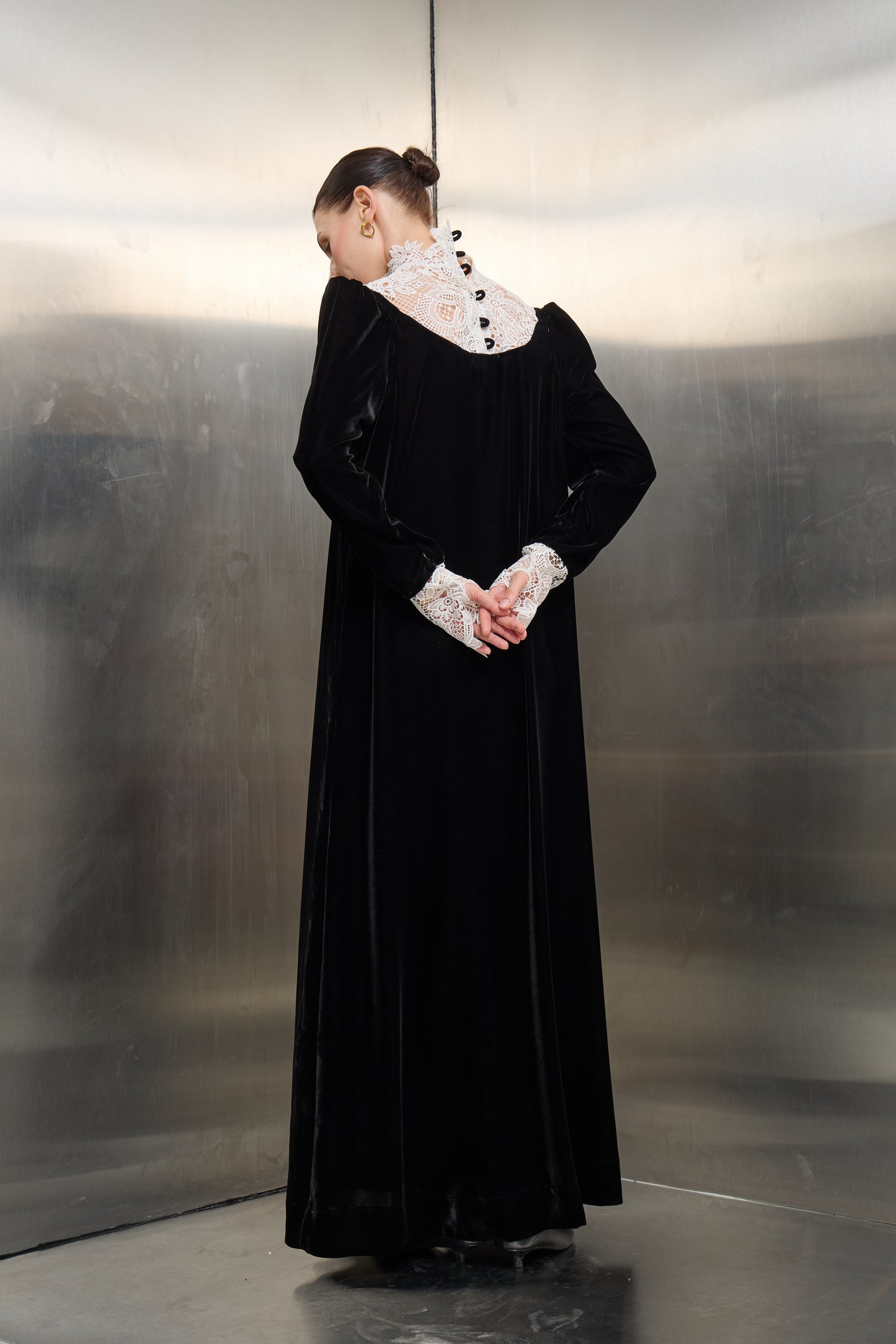 Rear view detail of the black velvet kaftan by Mona Al Shebil, showcasing the intricate white lace back panel with elegant button closures