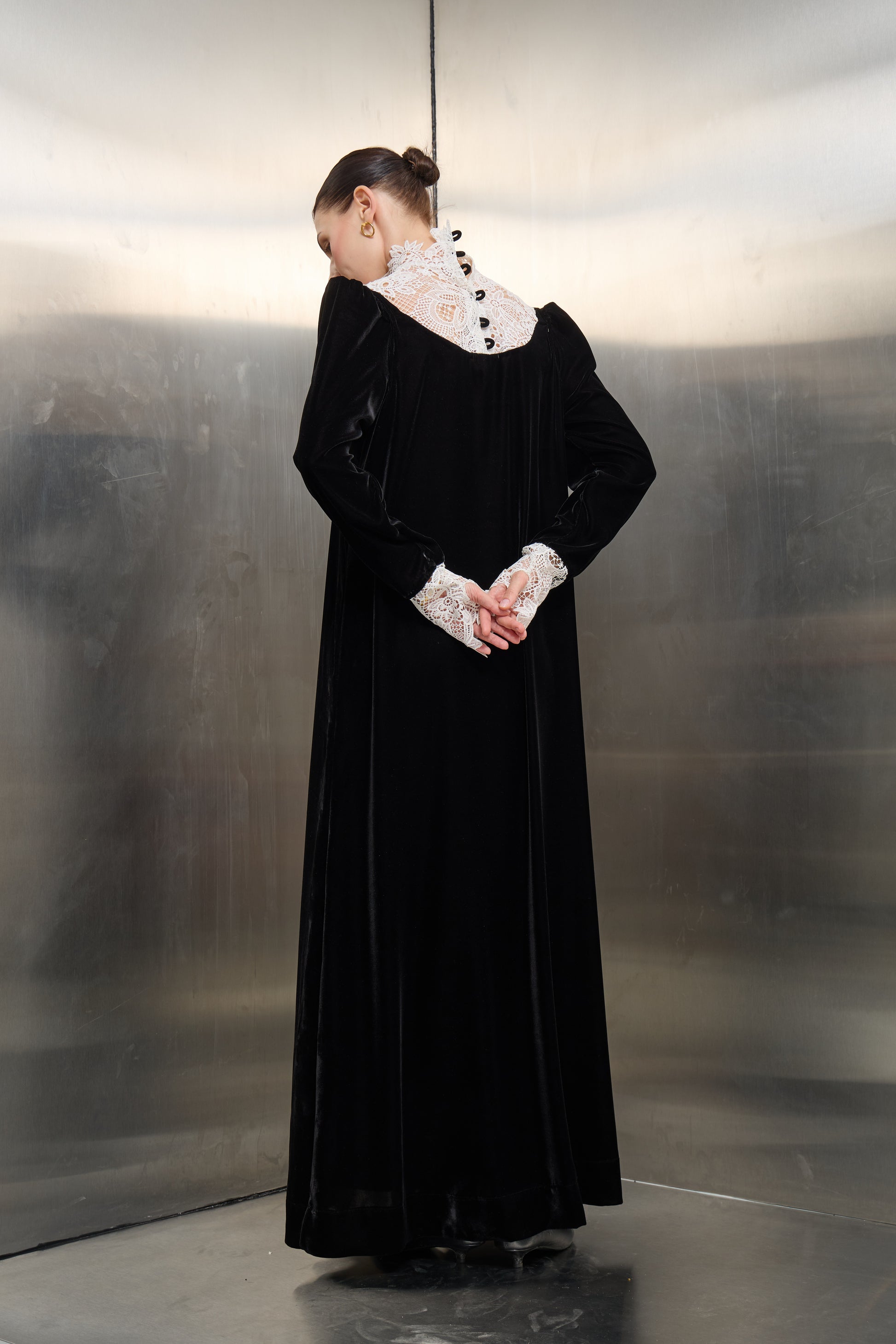 Rear view detail of the black velvet kaftan by Mona Al Shebil, showcasing the intricate white lace back panel with elegant button closures
